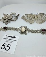 Three silver filigree jewelry pieces displayed on white background