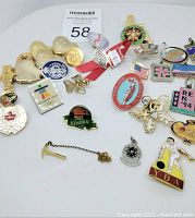 Photo showing a variety of pins and pendants arranged on a flat surface including a red and white origami crane, Rotary Club pins, US flag, and other assorted designs