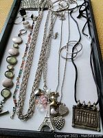 Top view of various fashion jewelry pieces arranged on a tray, including necklaces, charm pendants, rings, and bracelets.