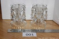 Pair of clear cut crystal candle stick holders with teardrop prisms, placed on a wooden surface with a ruler for size reference.