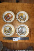Set of four decorative songbird plates arranged on wooden surface with ruler for size reference.