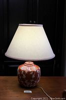 Front view of the 1970s burnt orange ceramic lamp with white shade on a wood surface.