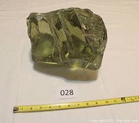 Large clear molten glass chunk placed on a white cloth with a measuring tape showing approximately 10 cm length.