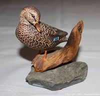 Front angled view of the hand carved mallard duck sitting on a wood and stone base.