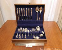 Full view of silver plate flatware set including knives, forks, spoons and serving pieces in wooden chest with blue felt interior.