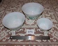 Three Federal Fire-King bowls in varying sizes placed on lace tablecloth next to a measuring ruler showing approximate sizes.