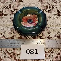 Top view of octagonal ashtray showing pink anemone flower with blue center on green background, with measuring ruler showing approx 4.5 inch width