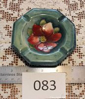 Octagonal ashtray with clematis design, placed on lace fabric with ruler showing width over 4.5 inches with damage indicated by a visible repair line
