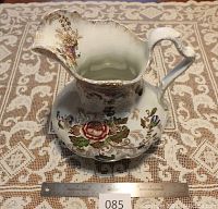 Water pitcher with floral transferware pattern and scalloped body seen from an angle. Ruler for scale in front of pitcher.