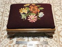 Top view of the antique needlepoint footstool showing detailed floral needlepoint upholstery over a wooden base with carved legs.