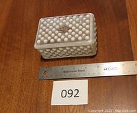 White milk glass hobnail dots on clear glass soap dish with lid, placed next to stainless steel ruler for size reference.