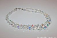 Double strand clear faceted beads necklace with Aurora Borealis multi-color reflections laid out on flat surface.