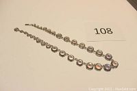 Photo shows a single strand necklace with graduated round beads featuring Aurora Borealis multi-colored reflective finish laid out flat with hook clasp visible.