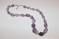 Full view of amethyst necklace laid out showing polished purple stones and metal clasps.