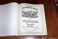 Photo of open book showing title page with decorative emblem and text: Illustrated Historical Atlas of Peterborough County 1825-1875, published by The Peterborough Historical Atlas Foundation Inc.