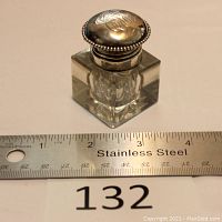 Inkwell with stainless steel ruler for size reference, showing cubed cut crystal bottom with beveled edges and hinged silver lid with monogram.