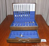 Full view of the complete flatware set arranged inside the opened wood storage chest showing upper and lower drawer compartments.