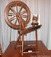Front view of wooden spinning wheel showing the large 21 inch diameter wheel, foot pedal, and flyer assembly with wood pegged joints.