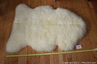 Top view of creamy white sheepskin rug with measuring tape showing approximate width 46 inches on hardwood floor.