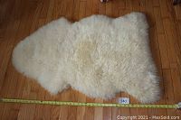 Top view of the creamy white sheepskin rug laid flat on wooden floor, measuring tape showing approx. 43 by 30 inches.