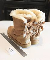 Pair of tan UGG boots showing back with lace-up bows and sheepskin lining at top, ruler beside for scale.