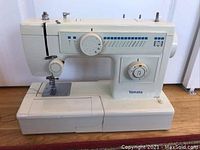 Front view of Yamata sewing machine showing stitch pattern selector, dials, needle area, and base with extension table.