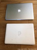 Two Apple laptops – one silver MacBook Pro and one white MacBook, closed view