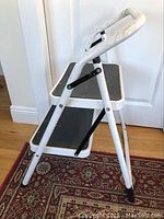Side view of white metal 2-step ladder showing black steps and curved handle