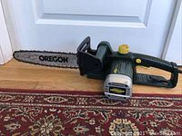 Side view of the Yardworks electric chainsaw showing the full length of the 14-inch Oregon bar and chain, black and green body with yellow button