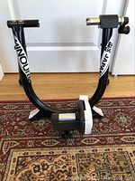Front view of the black steel bike trainer stand with visible Minoura and Magturbo 60 branding on the frame, showing structural frame and resistance unit.