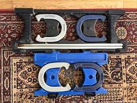 Top view of two pairs of Eastpoint branded metal horseshoes in grey and blue colors with two metal stakes placed on top of the blue carrying case.