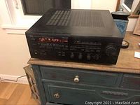 Front and angled view of the Yamaha RX-V970 receiver on a wooden table showing its digital display lit up and controls visible