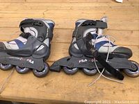 Side angle view showing both rollerblades together on wooden surface, displaying brand and wheel condition.