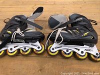 Side view of inline rollerblades showing black and gray boots, white metal frame with yellow wheels, and adjustable straps.