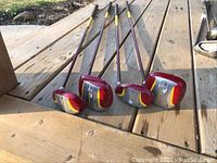 Angle showing five Navigator brand ladies golf clubs with red, yellow, silver club heads and brown/yellow shafts on wooden surface.