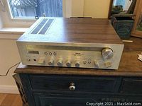 Front angled photo of Akai stereo receiver showing wood grain top and brushed metal front panel with control knobs and switches.