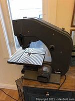 Side angle photo showing full band saw with metal construction, work table, and blade housing