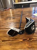 Full view of TaylorMade SuperFast Burner rescue club with headcover on wooden table.