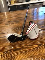 Photo of TaylorMade Burner Rescue golf club lying on wooden table with headcover next to it.