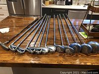 Complete view of 12 golf clubs laid out on a table, showing club heads and grips.