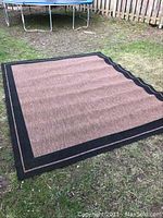 Outdoor rug laid flat on grass showing full design and color, highlighting condition and size