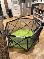 Hexagonal playpen with mesh sides and green floor pad shown in indoor setting.
