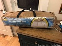 Brown carrying bag containing the 10x10 feet screen house tent with product label showing on side.