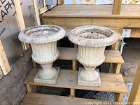 Pair of fiberglass urn-shaped planters placed on wooden steps, showing overall condition and design details such as fluted body and square bases.