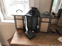 Photo of three AR wireless outdoor speakers and one wireless transmitter/receiver unit with antenna on a wooden surface near a window.