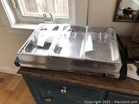 Front angled view of Oster buffet server with clear lids over compartments, showing control knob and indicator light on front right side.