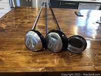Three right-handed golf drivers from different makers on a wooden table.