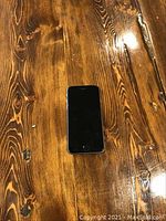 Front view of Apple iPhone 6s on wooden surface, screen off.