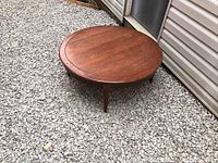 Full view of the vintage solid wood round coffee table on gravel showing top surface and legs.