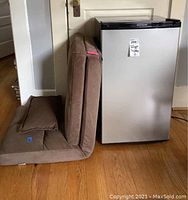 Photo showing the brown fabric folding futon chair in chair position next to the mini refrigerator.